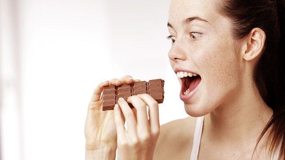Frau beißt herzhaft in eine Tafel Schokolade