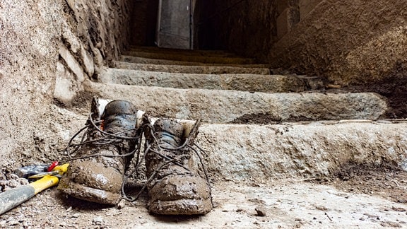 Abgetragene, schlammige Schuhe auf einer bröckeligen Treppe