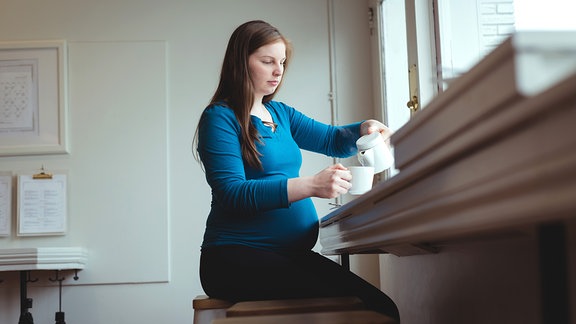 Eine junge, schwangere Frau gießt sich eine Tasse Kaffee ein