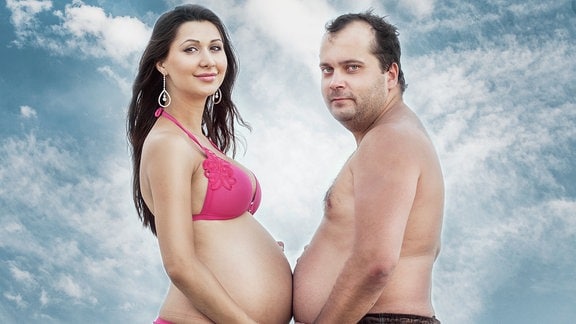 Schwangere Frau und Mann mit dickem Bauch in der selben Pose ihren Bauch umfassend.