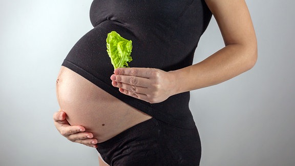 Eine Schwangere hält ein Salatblatt in der Hand.