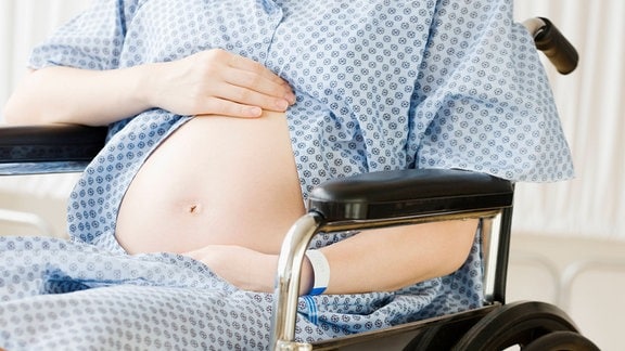 Eine schwangere Frau sitzt im Rollstuhl