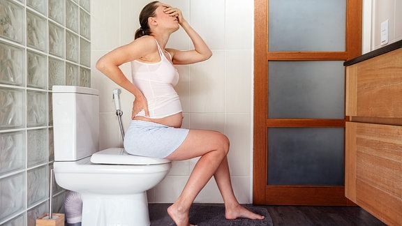 Illustration - Eine Schwangere mit Rückenschmerzen sitzt auf der Toilette