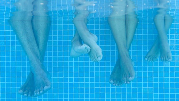 Unterwasseraufnahme zeigt vier Paar Füße im Wasser am Beckenrand.