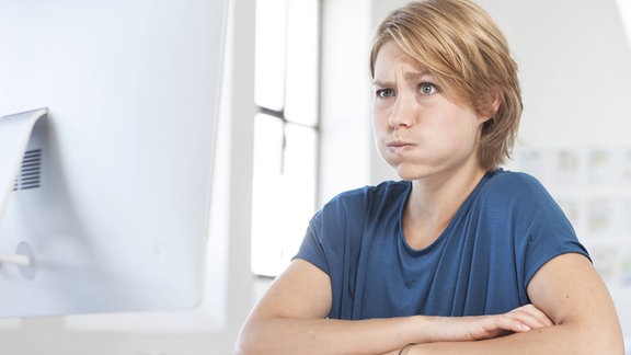 Porträt einer jungen Frau, die an ihrem Schreibtisch in einem Büro mit ihrem Mund schmollt.