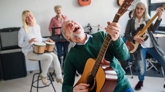 Gruppe vier mittelalter und älterer Menschen mit Musikinstrumenten, im Vordergrund Mann mit Gitarre, nach hinten gebeugt, in der musik schreiend 