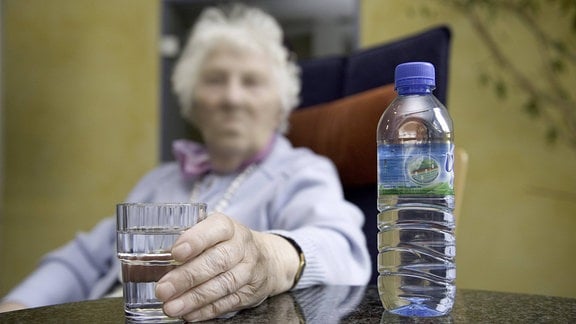 Eine Bewohnerin eines Pflegeheims sitzt mit einer Flasche Wasser im Aufenthaltsraum