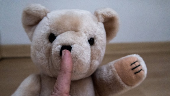 Symbolbild für sexuelle Gewalt: Teddybär, vor dessen Gesicht ein Finger zum Schweigen mahnt