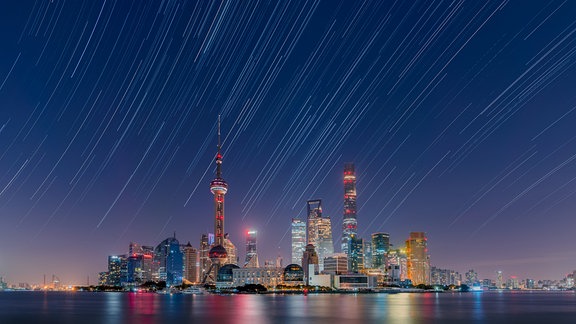 Dieses Bild zeigt Sternenspuren über Lujiazui City im Bezirk Pudong, und man kann sogar den Gürtel des Orion erkennen. Lujiazui ist der wohlhabendste Stadtteil in Schanghai, und die Lichtverschmutzung ist sehr stark, aber wenn das Wetter klar ist, kann man die Sterne sehen. Der Fotograf hat dieses Foto in einer sehr klaren Herbstnacht aufgenommen.