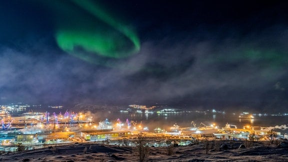 Das Polarlicht in Murmansk einzufangen, war für den Fotografen aufgrund der hellen Lichter in der Stadt kein leichtes Unterfangen. Um die Aurora Borealis in Murmansk zu fotografieren, muss man auf eine sehr starke Sonneneruption warten. Der Fotograf konnte nach mehreren Versuchen und vielen Stunden des Wartens die Aurora über der Kola-Bucht einfangen und wollte dieses optische Phänomen in einer Stadtlandschaft zeigen.