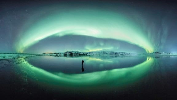 Dies ist ein 250-Grad-Panorama der Aurora Borealis in Island. Der Fotograf stieß auf diesen Strudel, der den Himmel in einer weit unter dem Gefrierpunkt liegenden Winternacht perfekt reflektierte, und nahm zuerst das Panorama auf und dann eine Aufnahme von sich selbst auf dem Eis. Für den Fotografen ist dies eines der erstaunlichsten Aurora-Bilder, das er je aufgenommen hat, und es fasst eine ehrfurchtgebietende Reise nach Island im Winter zusammen, die auch das Gefühl unterstrich, nur ein winziger Teil der Existenz des Planeten angesichts einer sehr mächtigen natürlichen Umgebung zu sein. Das Panorama besteht aus zwanzig Bildern, zwei Zehnerreihen, die mit einer Canon 5DMk3 und einem Canon 16-35mm aufgenommen wurden.