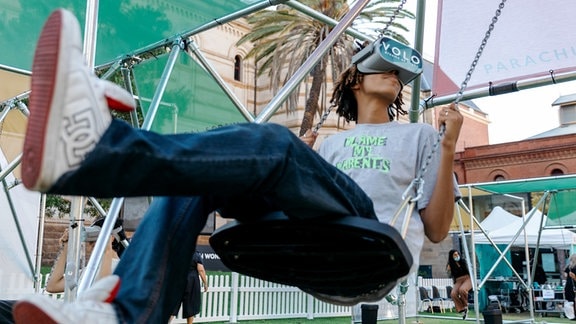 Ein junger Mann auf einer Schaukel mit VR Brille.