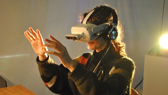Eine Frau mit VR-Brille fasst vor sich in die Luft. 