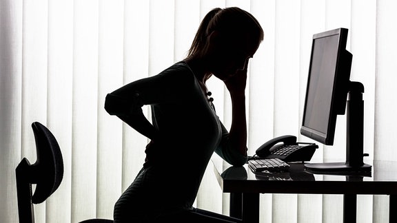 Silhouette einer Frau am Schreibtisch mit Rückenschmerzen.