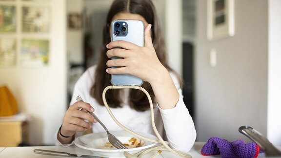 Eine Jugendliche schaut beim Essen auf ihr Smartphone.