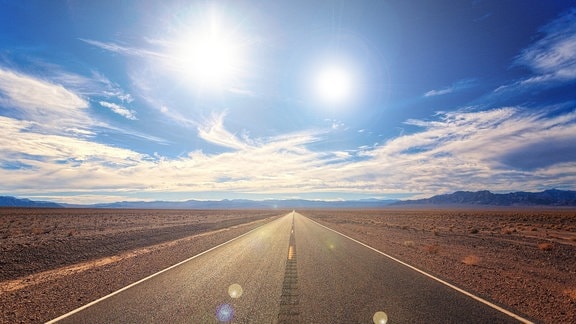 Fiktive Darstellung einer Landstraße durch die Wüste mit zwei mittig zum Betrachter strahlenden Sonnen am Himmel. Wolken am blauen Himmel. Leicht dramatische Stimmung.