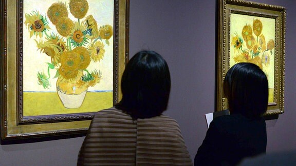 Besucherinnen einer Ausstellung betrachten zwei Sonnenblumen-Gmälde von Vincent van Gogh