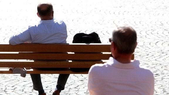 Zwei Männer sitzen einzeln auf zwei Bänken mit großem Abstand zueinander 