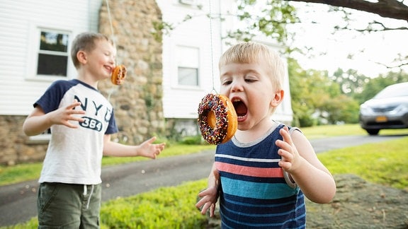 Zwei Jungen versuchen in Donuts zu beißen, die von einem Baum hängen