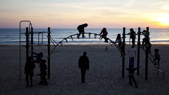 Kinder spielen bei Sonnenuntergang auf einem Spielplatz am Strand