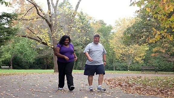 Eine Frau und ein Mann mit größerer Körperfülle laufen im Park.