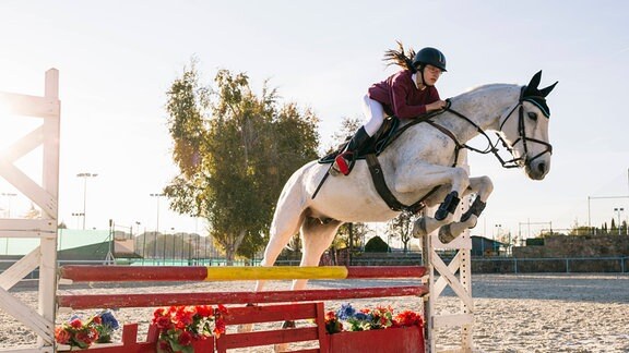 Teenager-Mädchen reitet auf einem weißen Pferd und trainiert für einen Hindernislauf 