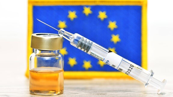 Impfspritze und Impfstoff-Fläschchen vor EU-Fahne