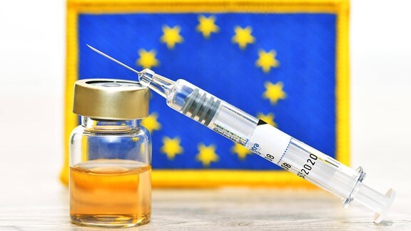 Impfspritze und Impfstoff-Fläschchen vor EU-Fahne
