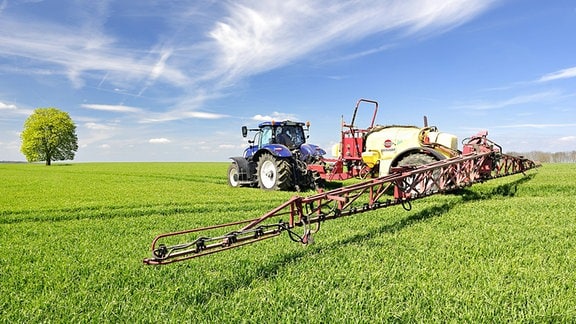 Traktor mit Feldspritze bringt Pestizide aus.
