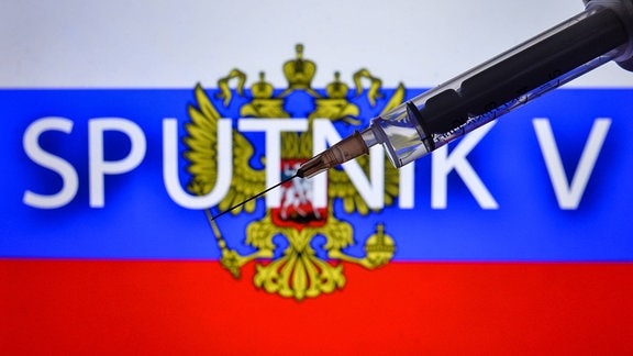Fotoillustration - eine medizinische Spritze und eine russische Flagge mit Sputnik V-Inschrift im Hintergrund.