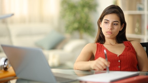 Unkonzentrierte Studentin sitzt gelangweilt vor ihrem Laptop