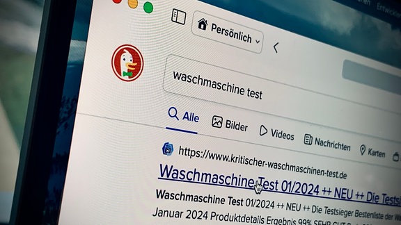 Ein schräg mit Unschärfe fotografiertes Browserfenster auf einem Laptop zeigt die Suchmaschine DuckDuckGo, die Suchbegriffe "Waschmaschine Test" und das wenig vertrauenswürde Suchergebnis "kritischer-waschmaschinentest.de"