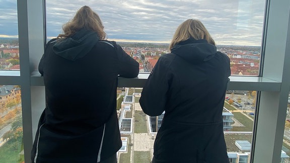 Zwei Teilnehmerinnen des Gründachkollegs schauen aus dem Hochhaus der MDR-Zentrale auf die recht kargen Gründächer der anderen Gebäudekämme.