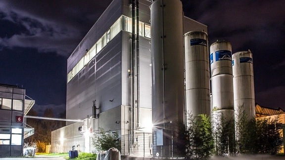 Eine Industriehalle vor der drei Silo-Türme stehen bei Nacht
