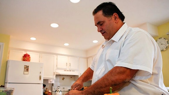 Übergewichtiger Mann schneidet Gemüse in einer Küche.