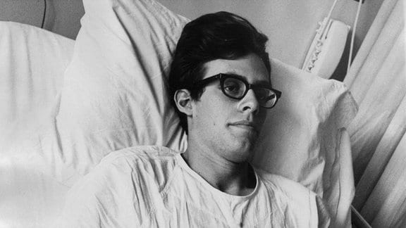 Schwarz/weiß Aufnahme. Ein Mann mit Brille in einem Krankenbett 