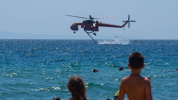 Ein Löschhubschrauber sammelt Wasser aus dem Meer.