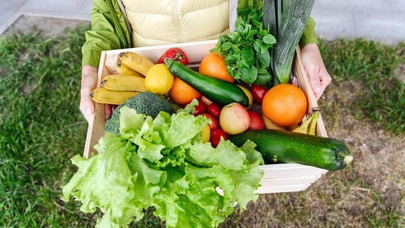 Eine Frau hält eine Kiste mit verschiedenem Obst und Gemüse