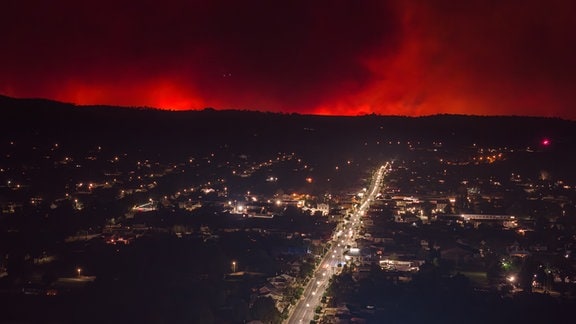 Flammen und Rauch von Buschbränden steigen hinter dem Stadtzentrum empor. 