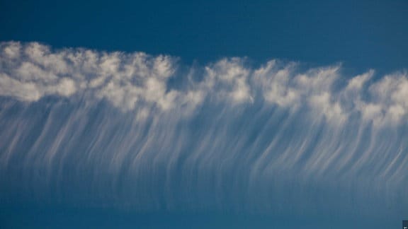 Diese Zirren bestehen aus Eiskristallen, die sich aufgrund der Sonnenerwärmung verändern und zu flockigen Wolken aufbauen. Die Wolkenströmung zieht die Gebilde auseinander.