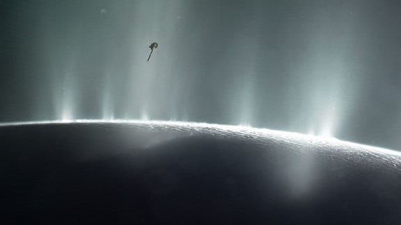 Die Raumsonde (oben) fliegt durch die Fontänen der Enceladus-Geysir. Der Mond befindet sich großflächig in der unteren Bildhälfte.