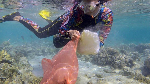 Frau in Tauchausrüstung schwimmt und sammelt Plastikmüll unter Wasser auf dem Boden des Korallenriffs.