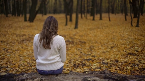 Frau sitzt alleine auf einem Stein im Wald