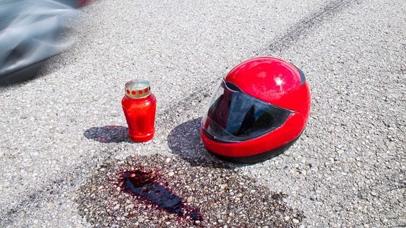 Blutfleck, Kerze und Motorradhelm auf einer Straße