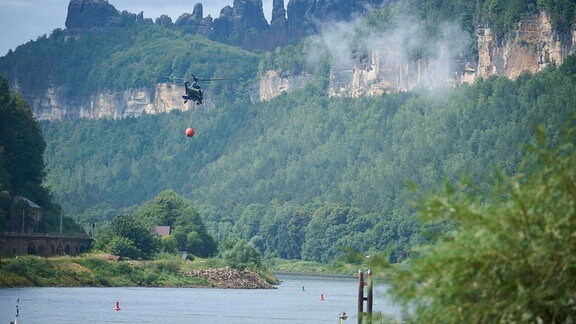 Ein Löschhubschrauber fliegt über einen Fluss in der Sächsischen Schweiz.
