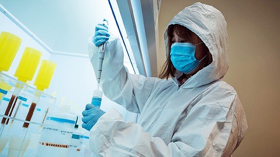 Eine Forscherin mit Mundschutz in einem Labor untersucht eine Porbe