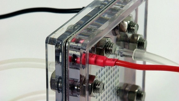 Brennstoffzelle, nahe Anischt, schräg/seitlich: Plexiglasgehäuser mit einer Art metallenem Gitter in der Mitte und verschiedenfarbeigen Kabeln und Schläuchen, die angeschlossen sind.