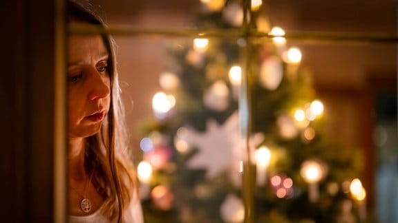 Inszeniertes Foto zum Thema Angst vor Einsamkeit am Heiligen Abend: Ein festlich dekorierter Weihnachtsbaum in einer Wohnung im Unterallgäu. Eine Frau schaut nachdenklich aus dem Wohnzimmer durchs Fenster.
