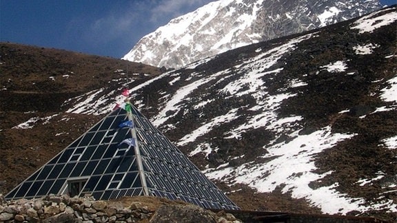 Eine Pyramide aus Solarzellen steht unterhalb eines schneebedeckten Berges.