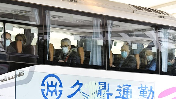 WHO-Mitarbeiter sitzen mit Maske in einem Bus in Wuhan.